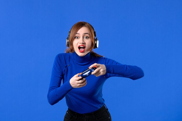 vue de face femme gamer avec casque et manette de jeu jouant à un jeu vidéo sur fond bleu canapé jeune fille gagnant vidéo adulte joie virtuelle