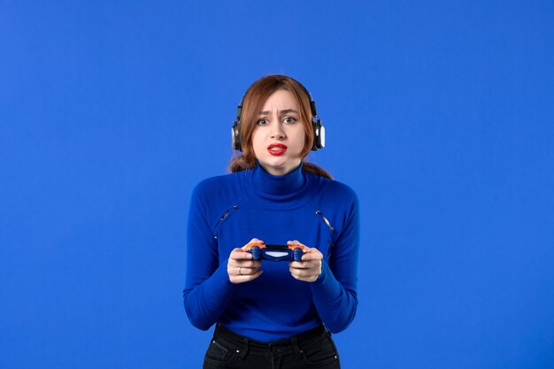 vue de face femme gamer avec casque et manette de jeu jouant à un jeu vidéo sur fond bleu fille jeunesse canapé joie gagnant lecteur vidéo adulte