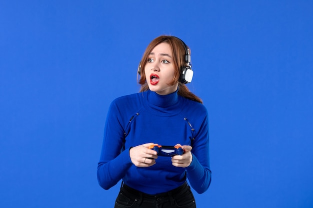 vue de face femme gamer avec casque et manette de jeu jouant à un jeu vidéo sur fond bleu jeune fille canapé gagnant joueur vidéo joie virtuelle