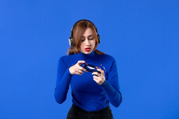 Photo vue de face femme gamer avec casque et manette de jeu jouant à un jeu vidéo sur fond bleu joueur fille jeunesse gagnant vidéo joie virtuelle jeune adulte canapé