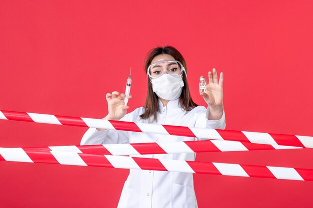 Photo vue de face femme médecin tenant une injection et une fiole sur fond rouge crime scellé ligne d'isolement de l'hôpital santé médical