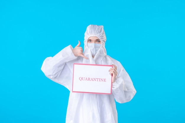 vue de face femme médecin en tenue de protection et masque tenant une écriture de quarantaine sur un bureau bleu virus médical pandémie de science de la santé