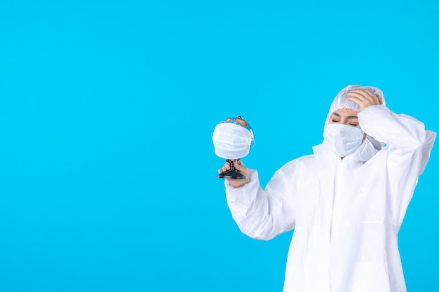 vue de face femme médecin en tenue de protection et masque tenant un globe masqué sur fond bleu science covid- virus pandémique couleurs médicales