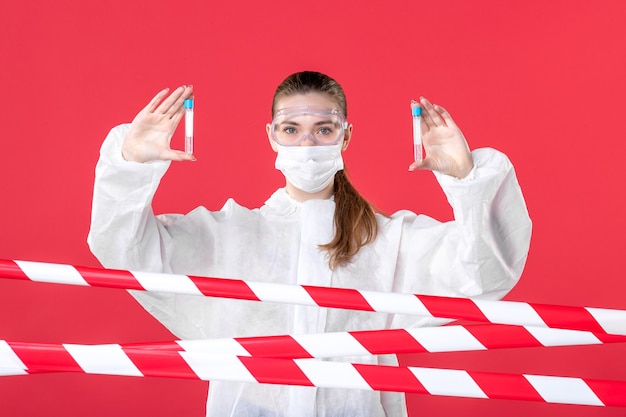 vue de face femme médecin en tenue de protection tenant des flacons sur fond rouge virus du crime covid- santé cure émotion infirmière de ligne hôpital