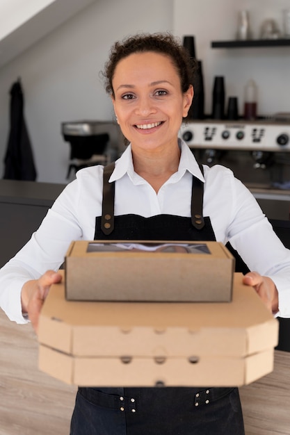 Vue de face d'une femme portant un tablier tenant des plats à emporter emballés