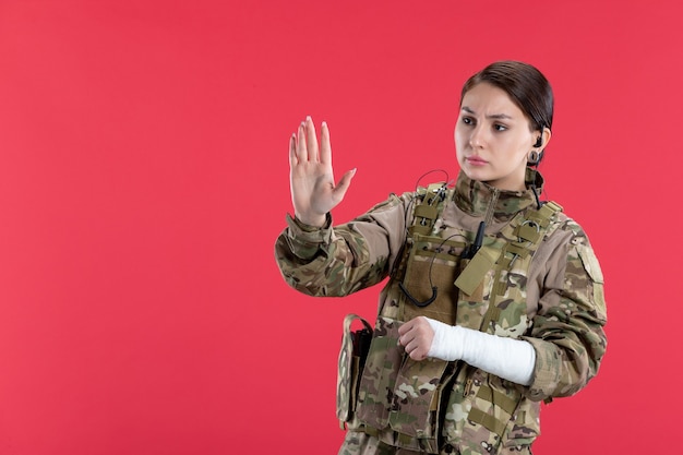 Vue de face femme soldat en camouflage avec mur rouge bras cassé