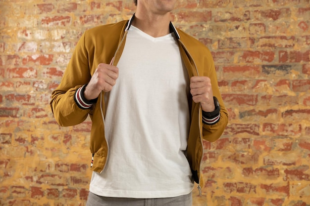 Vue de face gros plan d'un jeune homme de race blanche portant des vêtements de mode de rue décontractés tenant sa veste debout contre un mur de briques
