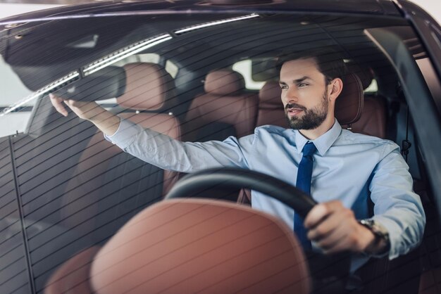 Vue de face de l'homme d'affaires ajustant le rétroviseur dans la voiture