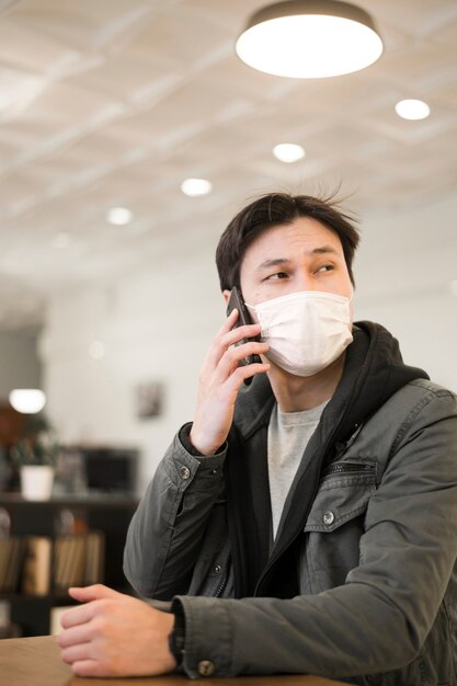 Vue de face de l'homme avec un masque médical parlant sur smartphone