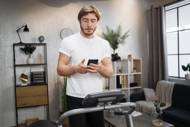 Vue de face d'un homme musclé sportif en t-shirt blanc tapant sur l'écran du smartphone