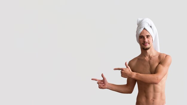 Photo vue de face de l'homme torse nu avec une serviette sur la tête pointant vers la gauche
