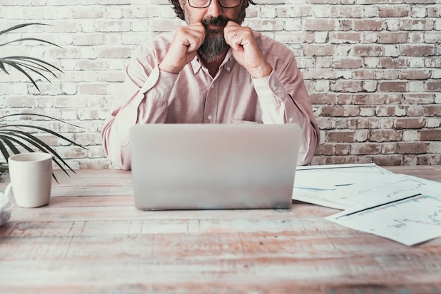 Vue de face d'un homme travaillant au bureau avec un ordinateur portable et des cartes papier Concept d'activité commerciale et professionnelle seule Table en bois avec des personnes utilisant un ordinateur pour gérer l'entreprise Un travailleur pensant à l'intérieur