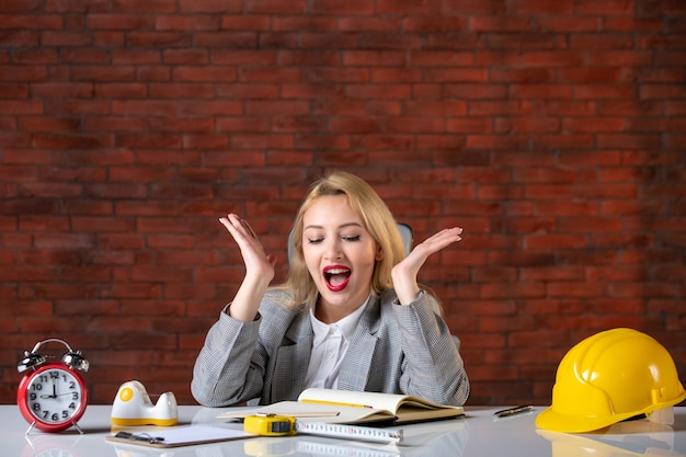 Vue de face ingénieur femme excitée assis derrière son lieu de travail