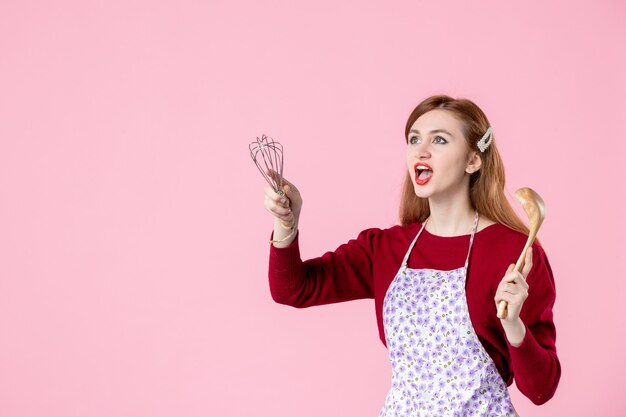 vue de face jeune femme au foyer avec cuillère et fouet en regardant quelque chose sur fond rose couleur douce cuisine femme nourriture gâteau tarte cuisine pâte cuisson