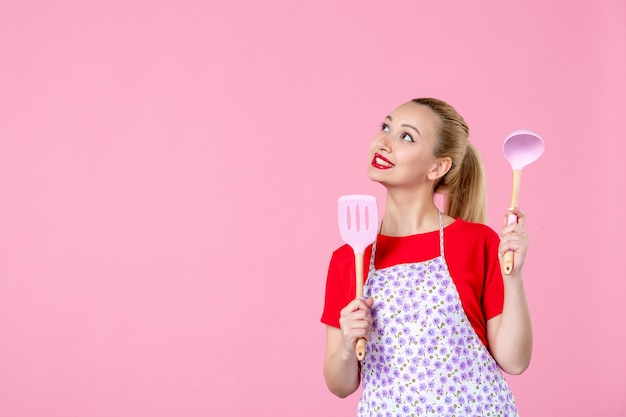 Vue de face jeune femme au foyer posant avec des couverts dans ses mains sur un mur rose