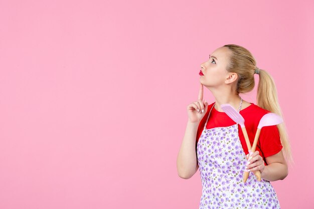 Vue de face jeune femme au foyer posant avec des couverts sur un mur rose