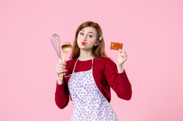 vue de face jeune femme au foyer tenant un fouet et une carte bancaire sur fond rose couleur douce cuisine cuisine femme gâteau nourriture