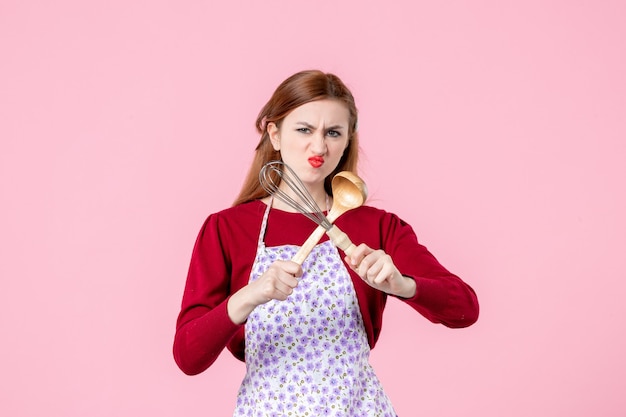 vue de face jeune femme au foyer tenant un fouet et une cuillère en bois sur fond rose cuisine profession pâte à tarte à tarte horizontale femme cuisson