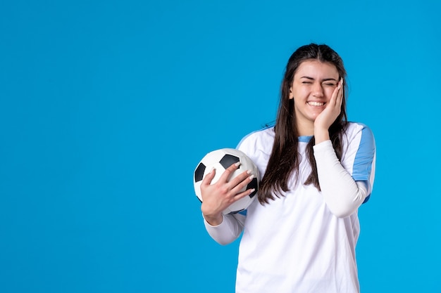 Vue de face jeune femme avec ballon de foot sur mur bleu