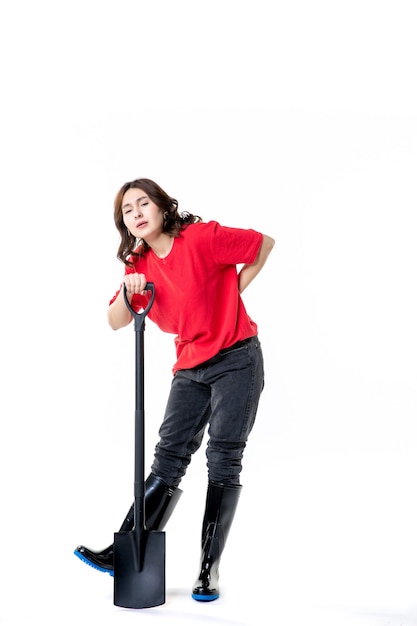 Vue de face jeune femme en chemise rouge tenant une pelle noire sur fond blanc travailler l'émotion du sol creuser la terre nature femme emploi