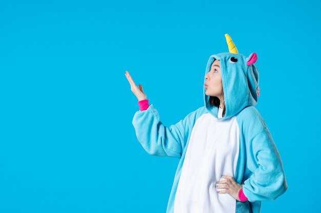 Vue de face jeune femme en kigurumi pour soirée pyjama sur fond bleu reste dormir tard dans la nuit jeu amis couleur du lit