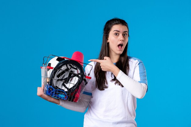 Vue de face jeune femme avec panier plein de choses de sport mur bleu