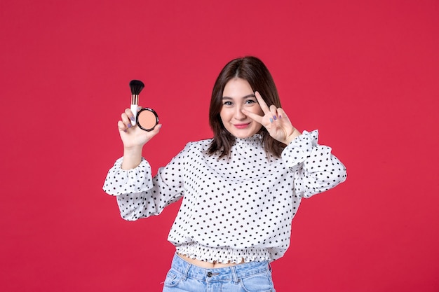 Vue de face d'une jeune femme avec pompon et poudre pour le maquillage sur mur rouge