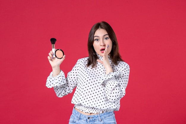 Vue de face d'une jeune femme avec pompon et poudre pour le maquillage sur mur rouge