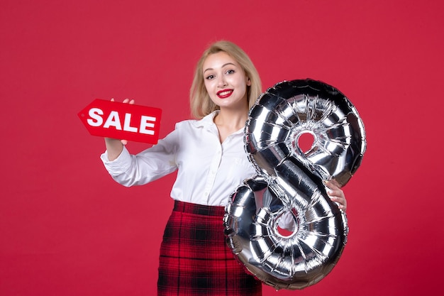 Vue de face jeune femme posant avec ballon d'argent et plaque signalétique de vente sur fond rouge égalité de la féminité affectueuse horizontale féminine