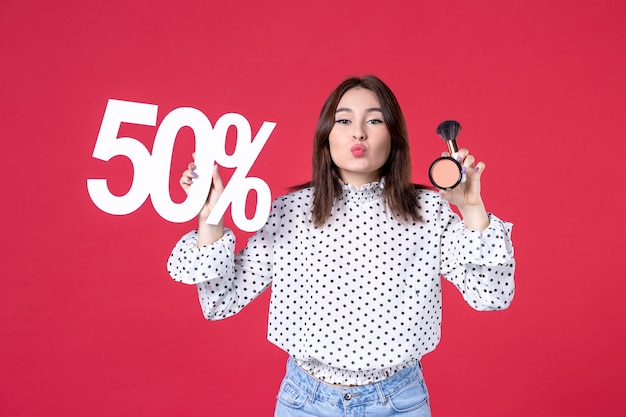 Vue de face jeune femme avec de la poudre de gland pour le maquillage et sur le mur rouge