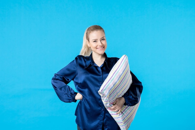 Vue de face jeune femme en pyjama holding oreiller sur fond bleu femme couleur sourire lit rêve cauchemar reste bâillement sommeil nuit