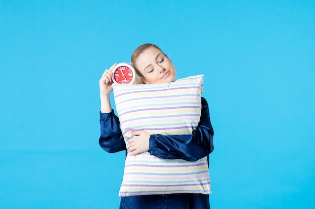 Vue de face jeune femme en pyjama avec réveil et oreiller sur fond bleu nuit partie repos sommeil femme fatiguée rêve cauchemar tard