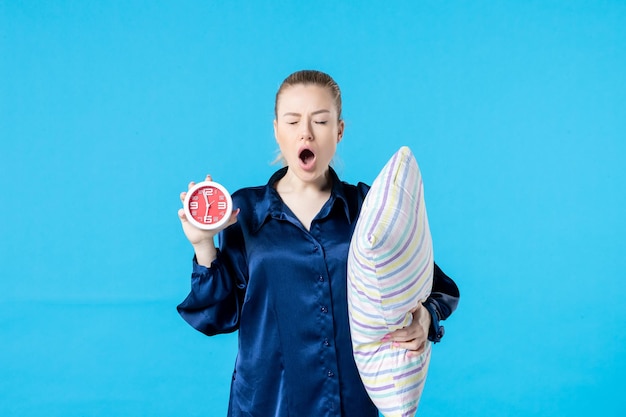 Vue de face jeune femme en pyjama avec réveil et oreiller sur fond bleu nuit repos sommeil fatigué femme tard rêve lit cauchemar