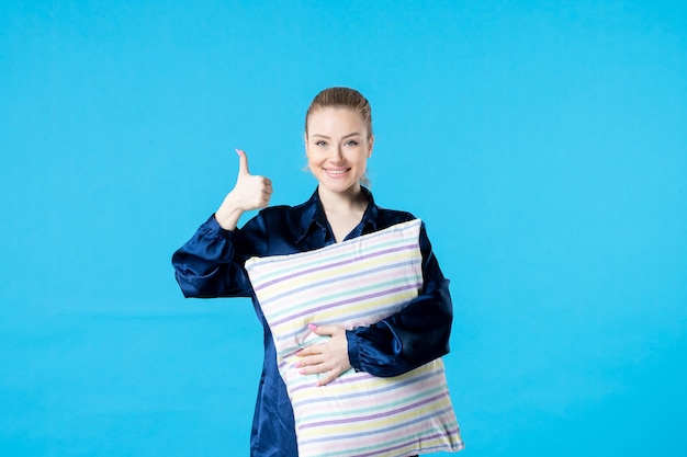 Vue de face jeune femme en pyjama tenant un oreiller sur fond bleu couleur sommeil cauchemar soirée rêve nuit repos fatigué lit bâillement