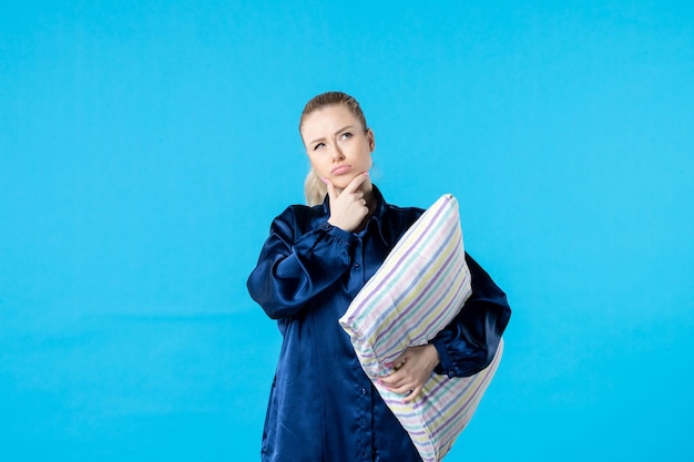 Vue de face jeune femme en pyjama tenant oreiller sur fond bleu femme couleur lit rêve pensée repos bâillement sommeil nuit