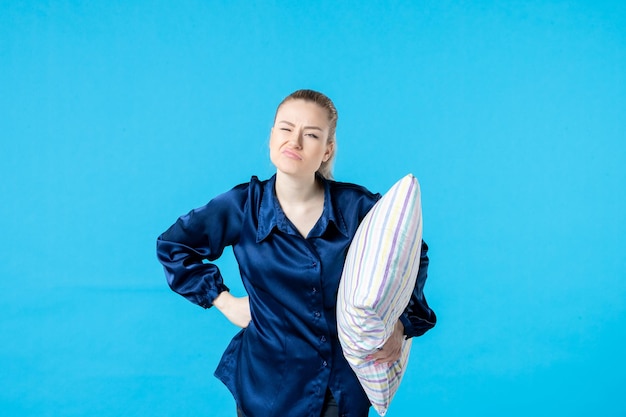 Vue de face jeune femme en pyjama tenant un oreiller sur fond bleu sommeil cauchemar fête rêve bâillement reste lit couleur nuit fatigué