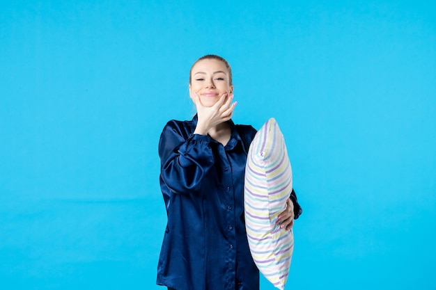 Vue de face jeune femme en pyjama tenant un oreiller sur fond bleu sommeil cauchemar parti rêve bâillement femme lit couleur nuit fatigué