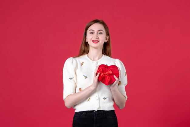 vue de face jeune femme tenant un cadeau en forme de coeur rouge sur fond rouge womens day shopping mall mode sensuelle égalité féminine