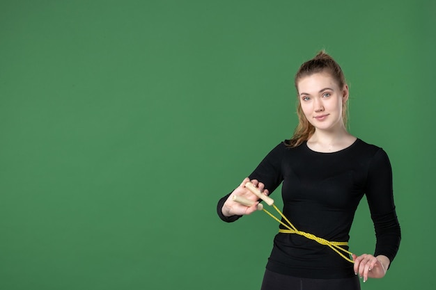 Vue de face jeune femme tenant une corde à sauter sur fond vert corps santé femme sport gymnastique athlète entraînement couleur