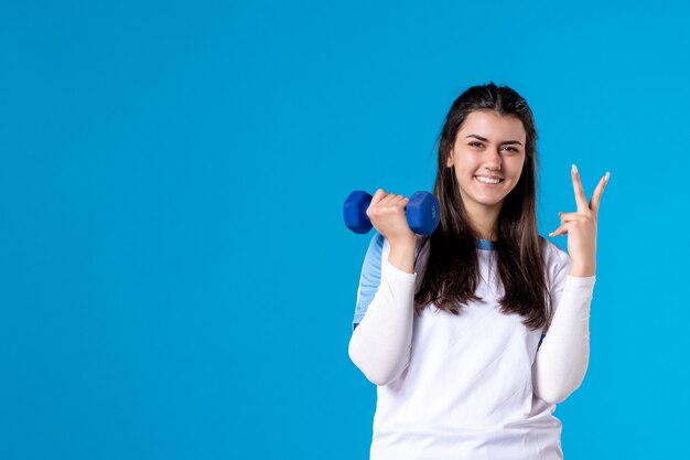 Vue de face jeune femme travaillant avec des haltères bleus sur mur bleu