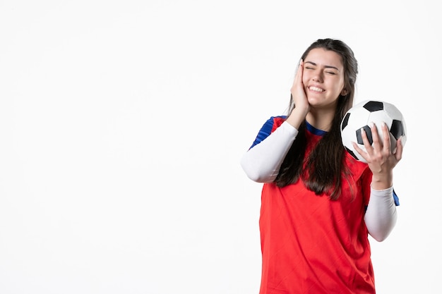 Vue de face jeune femme en vêtements de sport avec ballon de foot sur mur blanc