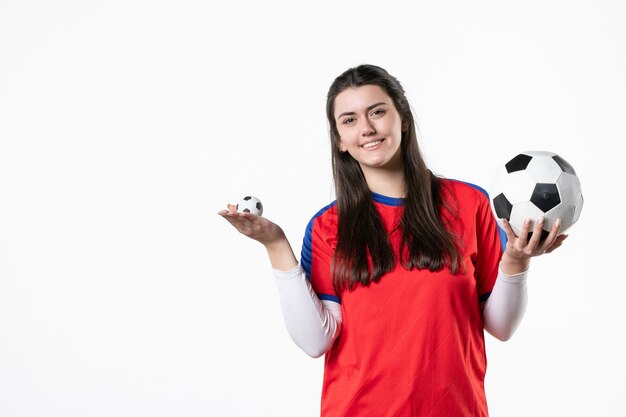 Vue de face jeune femme en vêtements de sport avec ballon de foot sur mur blanc