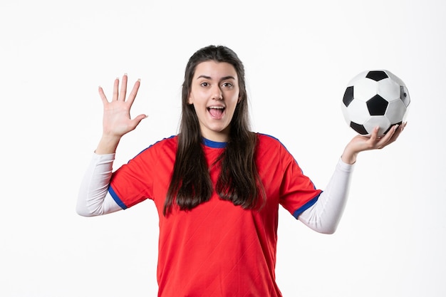 Vue de face jeune femme en vêtements de sport avec ballon de foot sur mur blanc