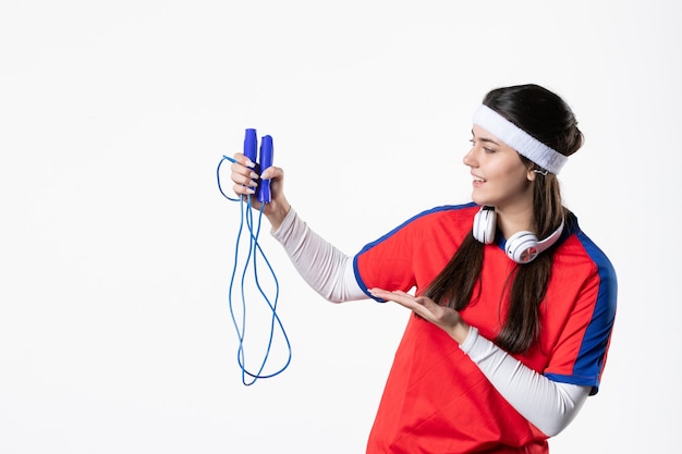 Vue de face jeune femme en vêtements de sport avec des cordes à sauter sur un mur blanc