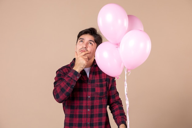 Vue de face jeune homme avec des ballons roses sur mur marron