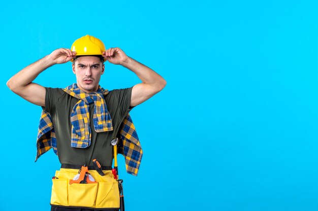 Vue de face jeune homme builder avec casque jaune sur fond bleu maison constructeur architecture bâtiment outils couleur travailleur plat