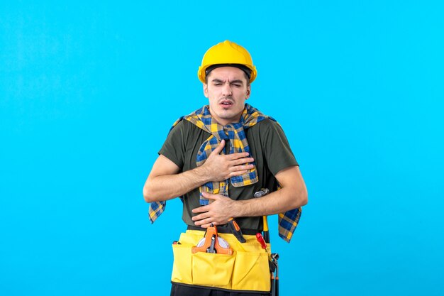 Vue de face jeune homme builder en casque jaune se sentant malade sur fond bleu couleur de l'outil architecture bâtiment constructeur travailleur du bâtiment