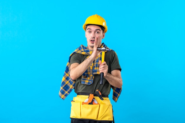 Vue de face jeune homme builder holding hammer sur fond bleu maison de travailleur architecture constructeur bâtiment plat