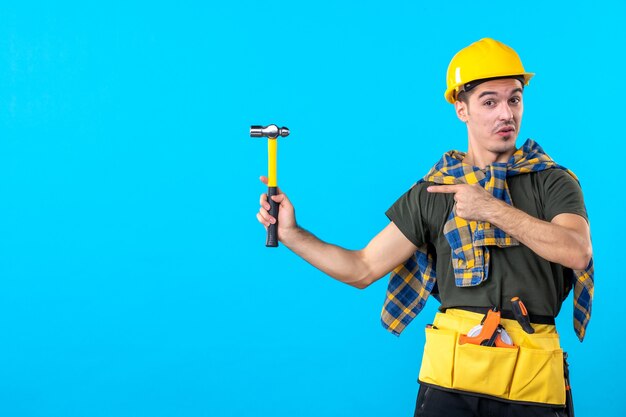 Vue de face jeune homme builder holding hammer sur fond bleu travail maison ouvrier architecture bâtiment plat