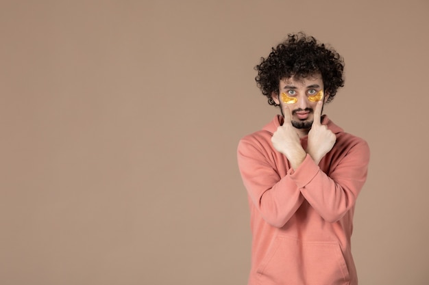 vue de face jeune homme avec cache-œil sur fond marron massage de la peau beauté du visage soins de la peau